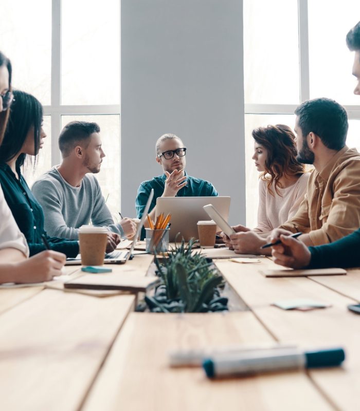 Staff meeting. Group of young modern people in smart casual wear discussing something while working in the creative office Staff meeting. Group of young modern people in smart casual wear discussing something while working in the creative office
